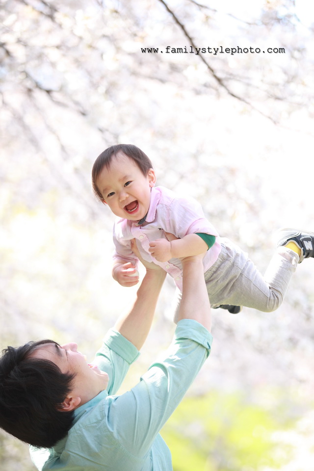 桜を背景にパパに高い高いをしてもらう笑顔の子供