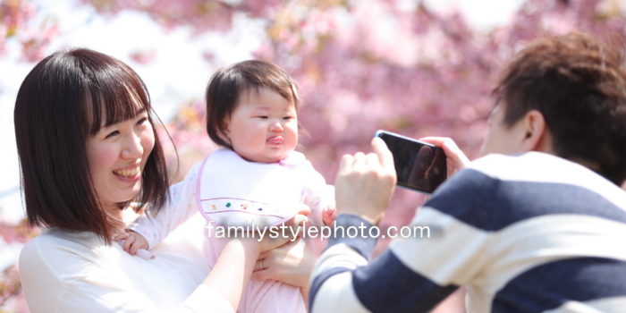 桜を背景にママと赤ちゃんの写真を撮るパパ